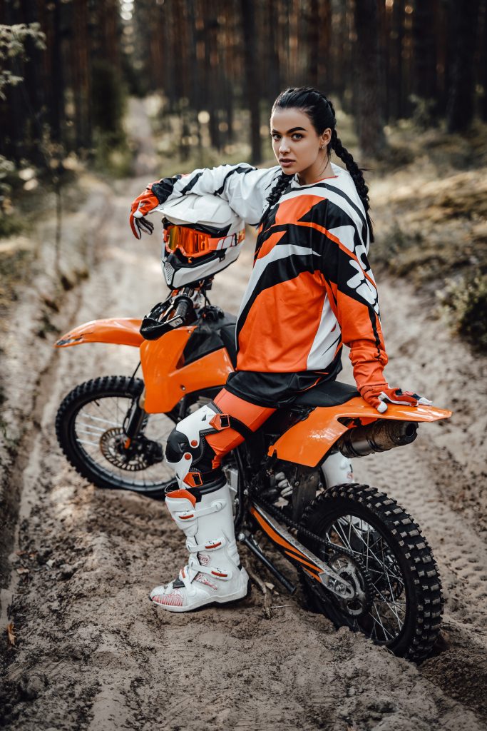 Beautiful young brunette female racer riding enduro bike on a trail of sand in the woods