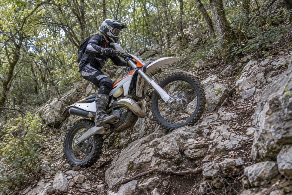 Two-stroke enduro rider climbing a steep rocky forest trail